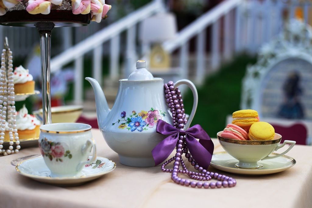 A beautiful porcelain tea set with cupcakes and macarons, adorned with pearls and lavender ribbon, for an elegant tea time.